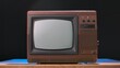 © kinomaster - Old TV on a wooden table against black studio background. Brown retro media equipment. Retro TV with a turned off screen. An aged analog apparatus for broadcasting entertainment programs.