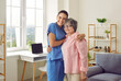 © Studio Romantic - Happy beautiful senior woman together with her friendly young nurse or caregiver standing in room in retirement home, hugging each other, looking at camera and smiling
