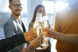 © maxbelchenko - Toasting to success concept.Group of young business people toasting each other and smiling while standing in the office. Celebration and festive concept.