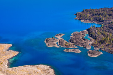 Wall Mural - aerial view of very blue and clear water with a jagged volcanic shoreline.