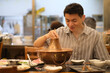 smiling Chinese young man eating Instant-boiled mutton hot pot in restaurant, a traditional Chinese hotpot