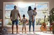 © David L/peopleimages.com - Family, love and window back view in home looking at mountain. Support, trust and baby, mother and father holding hands of girl in house with scenic view, enjoying quality time together and bonding.