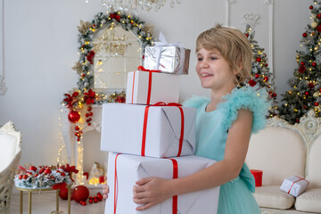 A teenage girl in a smart dress holds a large pile of Christmas gifts. The child received many gifts. Around New Year's Christmas decor