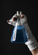 Mummy's hand wrapped in a bandage holds a laboratory flask with an elixir isolated on a black background. Halloween concept
