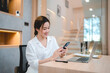© chokniti - Smiling young Asian business woman and entrepreneur using mobile phone and scrolling and browsing through social media on taking break after working on laptop
