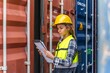 © asean studio - Photo of a young beautiful professional western female brunette engineer inspecting containers in a shipping containers yard to ensure the content and delivery information is correct