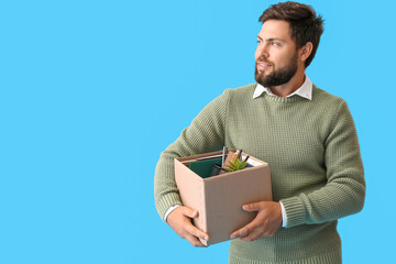 Poster - Smiling fired young man holding box with personal stuff on blue background