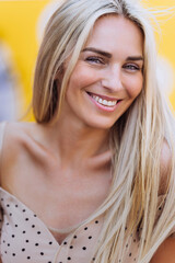 Vertical portrait of blonde Caucasian cheerful woman in beige dress toothy smiling looks at camera Happily satisfied spending time outdoors at summertime. Cheerful Student, beautiful fashion model.