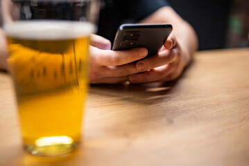 man hand hold smartphone, drinking beer and reading message at bar or pub