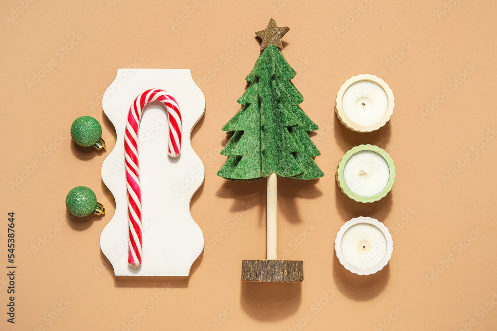 Decorative Christmas tree with podium, candy cane, candles and balls on beige background