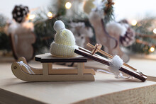 Small Wooden Sled, Skis And A Winter Hat, Christmas Tree Decorations On The Background Of A Christmas Tree