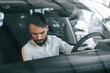 © standret - Inside of the automobile. Young man in white clothes is in the car dealership