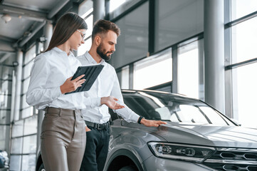 Wall Mural - Touching the automobile surface. Man with woman in white clothes are in the car dealership together