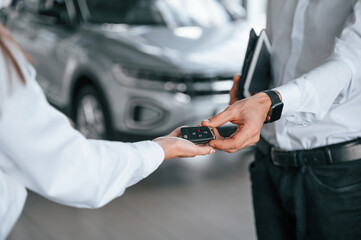 Wall Mural - Keys of new automobile. Close up view. Man with woman in white clothes are in the car dealership together