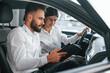 © standret - Sitting in the automobile. Man with woman in white clothes are in the car dealership together
