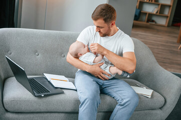 Wall Mural - Sitting on the sofa. Father with toddler is at home, taking care of his son