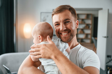 Wall Mural - Standing with baby in hands. Father with toddler is at home, taking care of his son