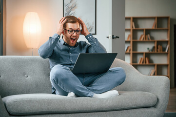 Wall Mural - Celebrating success. Male freelance worker is using laptop at home. Cozy apartment