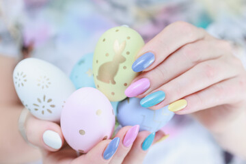 women's hands with multi-colored manicure hold easter eggs. light yellow, blue and pink color.