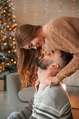 Wall Mural - Woman is standing and looking at her man from above. Lovely young couple are celebrating New Year at home