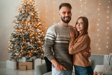 Wall Mural - Standing and smiling. Lovely young couple are celebrating New Year at home