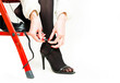 young woman feet in black shiny pantyhose and high heels on red ladder isolated on white background