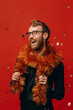 Red-haired cheerful man in glasses and golden boa at New Year party with confetti. Studio photo.