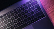 © Elena Uve - Desktop view of laptop keyboard with purple lights on wood table. Workplace. Work from home. Office desk.