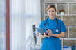 © ArLawKa - Smart and attractive Asian female doctor ready for surgery. a beautiful woman wearing a blue robe and standing medical and health concepts front view in doctor's office