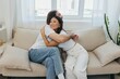 © SHOTPRIME STUDIO - A man and a woman are sitting on the couch at home wearing white T-shirts and hugging each other with smiles. Family life lifestyles of young marrieds