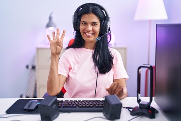 Poster - Mature hispanic woman playing video games at home showing and pointing up with fingers number four while smiling confident and happy.