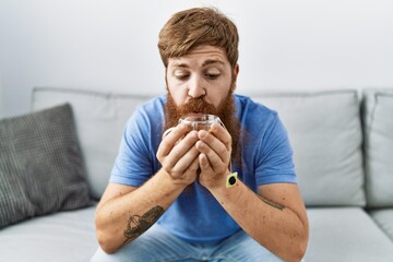 Poster - Young irish man blowing on cup of tea sitting on the sofa at home.