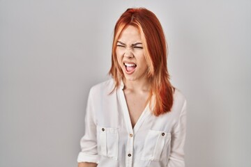 Sticker - Young caucasian woman standing over isolated background angry and mad screaming frustrated and furious, shouting with anger. rage and aggressive concept.