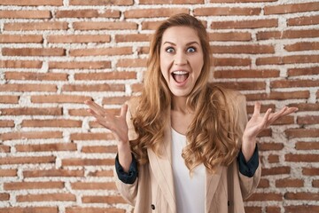 Poster - Beautiful blonde woman standing over bricks wall celebrating crazy and amazed for success with arms raised and open eyes screaming excited. winner concept