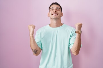 Wall Mural - Handsome hispanic man standing over pink background celebrating surprised and amazed for success with arms raised and eyes closed. winner concept.