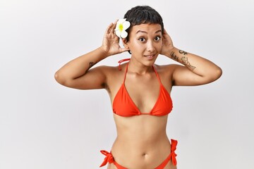 Wall Mural - Young hispanic woman with short hair wearing bikini trying to hear both hands on ear gesture, curious for gossip. hearing problem, deaf