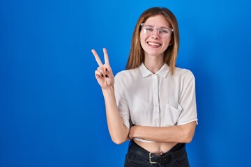 Poster - Beautiful woman standing over blue background smiling with happy face winking at the camera doing victory sign. number two.