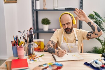 Canvas Print - Young bald man artist listening to music drawing on notebook at art studio