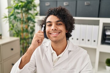 Wall Mural - Young hispanic man optician holding eye drop at clinic