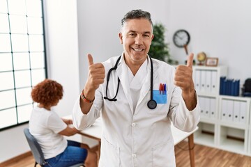 Sticker - Middle age doctor man at the clinic with a patient success sign doing positive gesture with hand, thumbs up smiling and happy. cheerful expression and winner gesture.