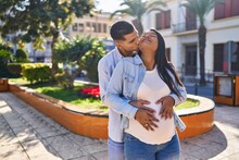 Young Latin Couple Expecting Baby Hugging Each Other And Kissing At Park
