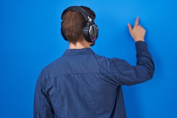 Poster - Hispanic man with beard listening to music wearing headphones posing backwards pointing ahead with finger hand