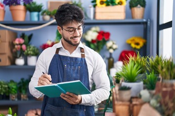 Wall Mural - Young hispanic man florist smiling confident writing on notebook at florist shop