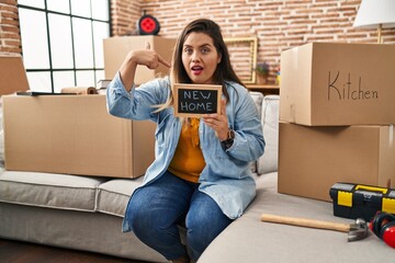 Wall Mural - Young hispanic woman holding blackboard with new home text pointing finger to one self smiling happy and proud