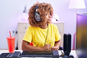 Canvas Print - Young hispanic woman with curly hair playing video games wearing headphones looking to side, relax profile pose with natural face with confident smile.