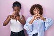 © Krakenimages.com - Two african women standing over pink background rejection expression crossing fingers doing negative sign