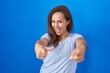 © Krakenimages.com - Brunette woman standing over blue background pointing fingers to camera with happy and funny face. good energy and vibes.