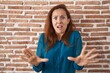 Brunette woman standing over bricks wall afraid and terrified with fear expression stop gesture with hands, shouting in shock. panic concept.