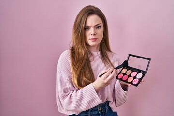 Poster - Young caucasian woman holding makeup brush and blush palette skeptic and nervous, frowning upset because of problem. negative person.