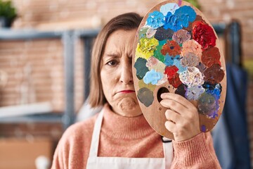 Sticker - Middle age hispanic woman holding painter palette close to face depressed and worry for distress, crying angry and afraid. sad expression.